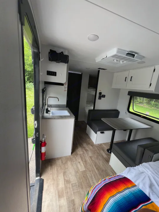 RV rental interior: kitchen, dinette, bunk beds, and AC visible. Bright space with a fire extinguisher by the open door.. Keystone RV Hideout 2023