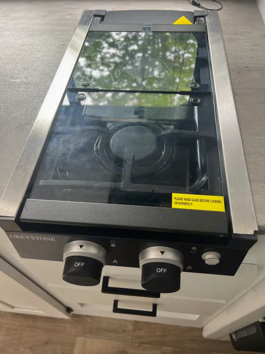 Greystone 2-burner gas cooktop in an RV rental. Its glass cover is closed, displaying a safety warning to raise it for cooking.. Keystone RV Hideout 2023