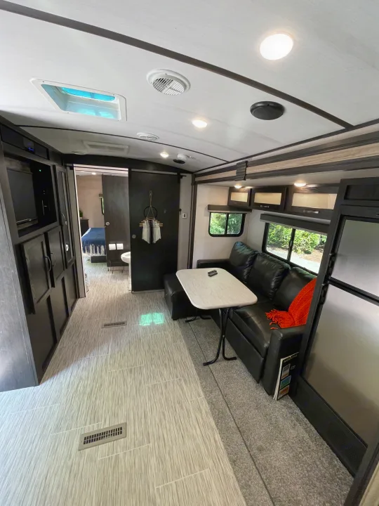 Modern RV rental interior. Living area features black sofa, table, storage, with a clear path to the bedroom and bath.. Forest River Surveyor Luxury 2020