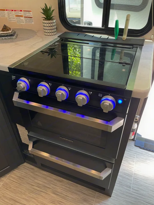 Modern Furrion gas range and oven with blue-lit controls in an RV rental, offering home-like cooking convenience.. Forest River Surveyor Luxury 2020