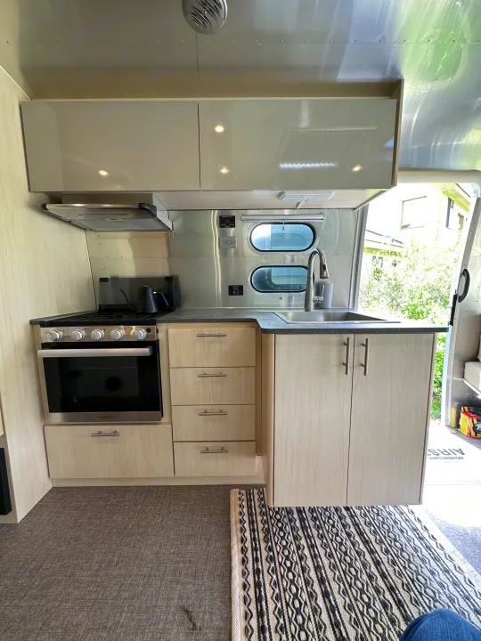 Inside an RV rental: a bright kitchen with stainless appliances, light wood cabinets, and aluminum walls.. Airstream Flying Cloud 2022