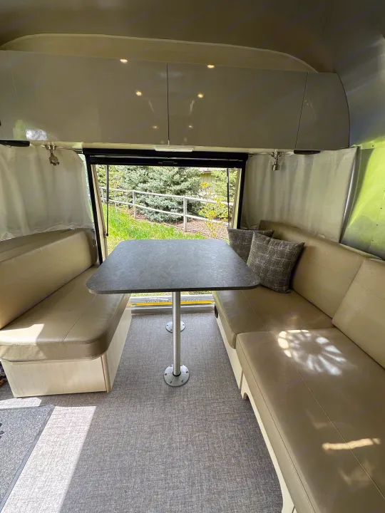 Cozy RV rental dinette area with a table & benches facing a scenic outdoor view. Light-colored interior.. Airstream Flying Cloud 2022