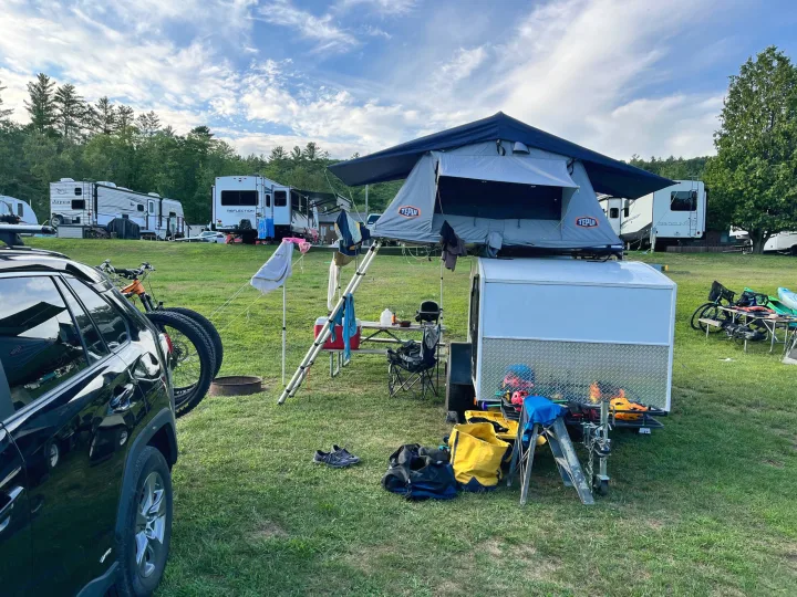 RV rental campground scene: a car, trailer with rooftop tent, and various RVs. Perfect for outdoor camping adventures.. Other Other 2020