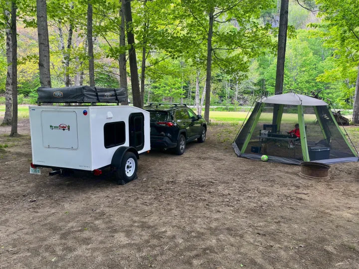 RV rental camping setup: a mini teardrop trailer with rooftop tent, SUV, & screen house in a lush, wooded campsite.. Other Other 2020