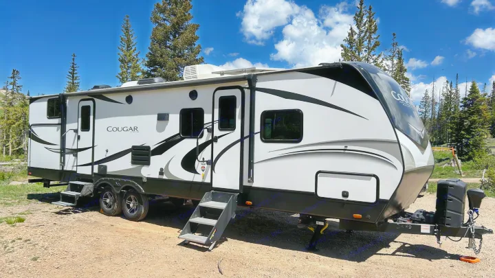 Explore nature with this Cougar travel trailer RV rental, set up at a beautiful campsite under a blue sky.. Keystone Cougar Half-ton 2022