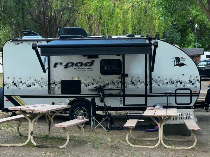 RV rental: An R-Pod travel trailer, with an extended awning, parked at a rustic campground with two picnic tables.. Forest River R POD 193  H.R. EDITION 2022