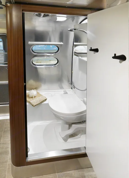 RV rental's compact wet bath: a toilet, shower, and unique oval windows looking out to the ocean. Functional and bright.. Airstream Caravel 2020