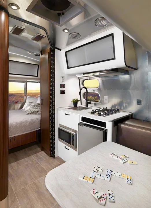 Explore this Airstream RV rental interior, featuring a compact kitchen, dining area with games, and a cozy bedroom.. Airstream Caravel 2020