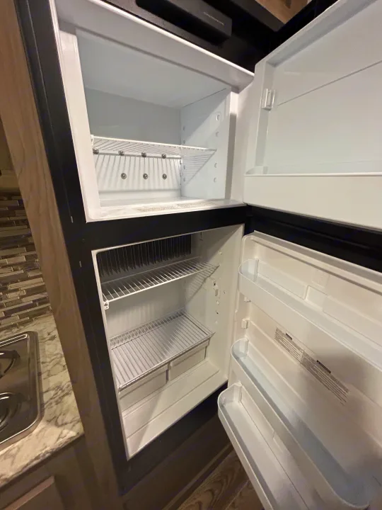 Clean, empty rv rental refrigerator. Features top freezer, lower fridge with wire shelves, crispers, and door bins.. Gulf Stream Ameri-Lite Super Lite 2021