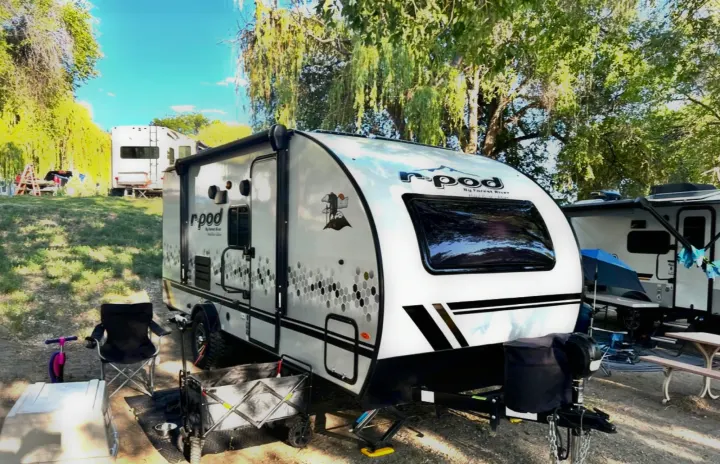 This RV rental, a white R-pod travel trailer, is set up at a sunny campsite with other RVs and outdoor gear.. Forest River R POD 193  H.R. EDITION 2022