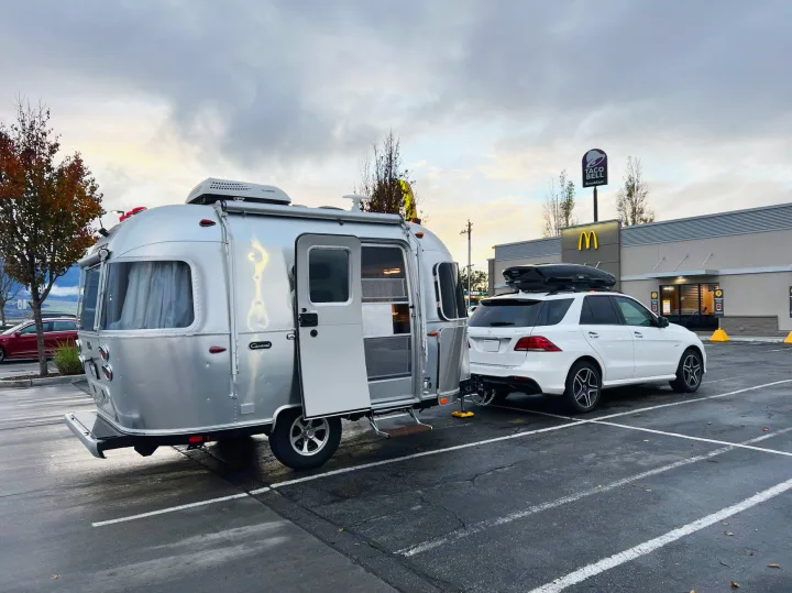 A white SUV tows an Airstream RV rental, parked outside McDonald's & Taco Bell under a cloudy sky. Ready for a road trip!. Airstream Caravel 2020