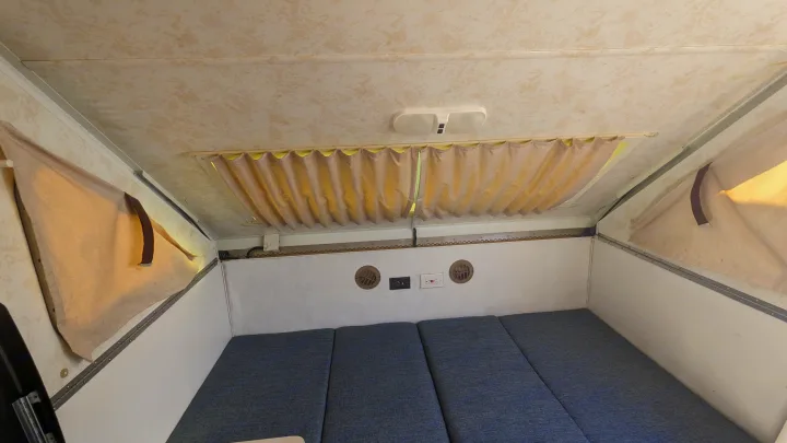 This RV rental's interior features a compact bed, privacy curtains, vents, and an overhead light.. Chalet Chalet Popup Trailer 2006