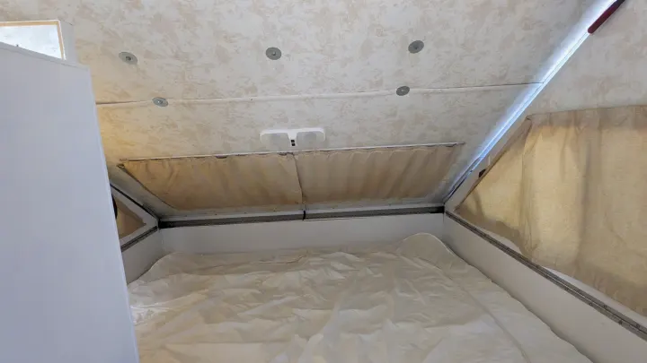 Inside an RV rental: a neat bed with white sheets, overhead light, and side curtains for privacy. Ideal for compact adventures.. Chalet Chalet Popup Trailer 2006