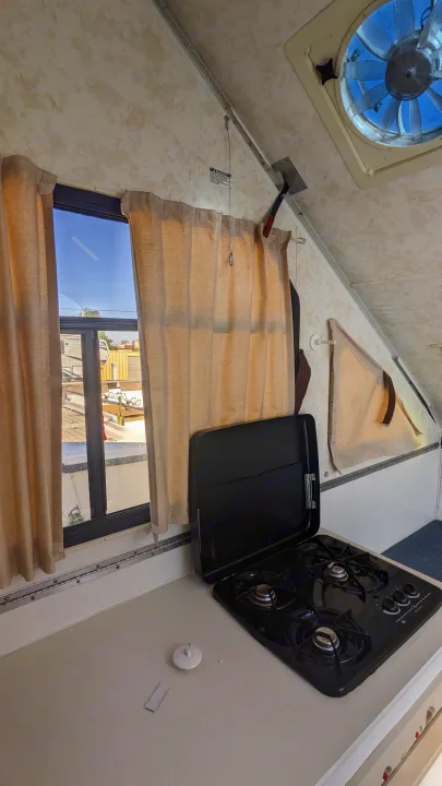 Inside an RV rental, featuring a compact kitchen with a gas stove, window, and ceiling vent fan.. Chalet Chalet Popup Trailer 2006