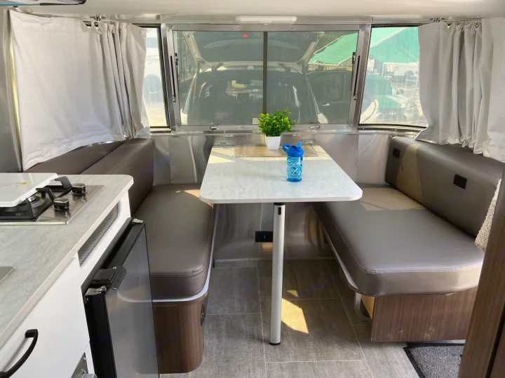 Spacious rv rental interior featuring a cozy dinette, compact kitchen with stove & fridge, and large windows.. Airstream Caravel 2020