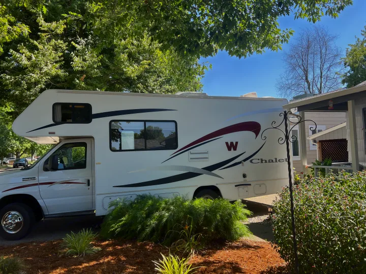 White Chalet RV rental motorhome parked beside a house, shaded by vibrant green trees, awaiting its next journey.. Winnebago Chalet 2010