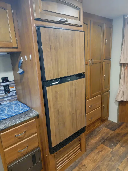 Inside an RV rental: detailed wood cabinetry, integrated Furrion refrigerator, and wood-look flooring create a cozy, functional space.. Keystone 27BHS 2017