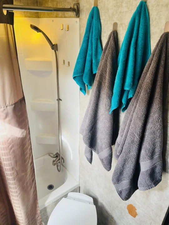 Inside an RV rental bathroom: a functional shower setup with a flexible hose and various towels hanging on wall hooks.. Highland Ridge RV Light 2017