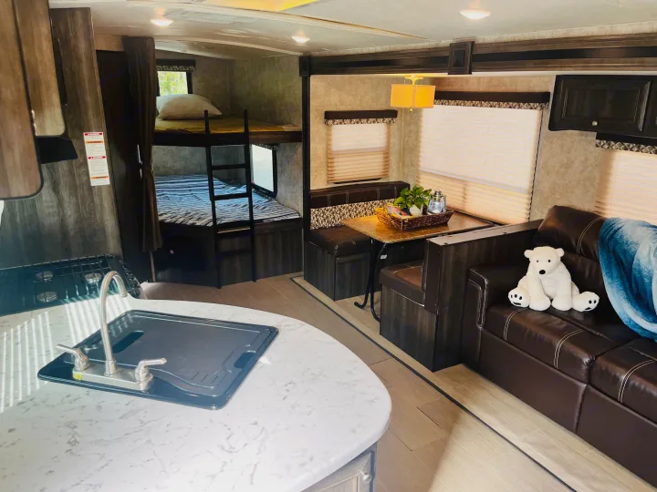 Spacious RV rental interior featuring a kitchen area, dining booth, comfy couch with a polar bear, and bunk beds.. Highland Ridge RV Light 2017