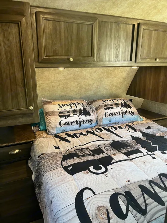 Cozy RV rental interior with "Happy Camping" bedding, wood-look cabinets, and a comfortable bed.. Highland Ridge RV Light 2017