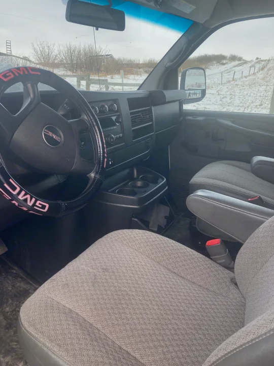 Inside a GMC van, a spacious RV rental option, featuring gray seats, dashboard, and steering wheel. Snowy view outside.. Gmc Savanna 2013