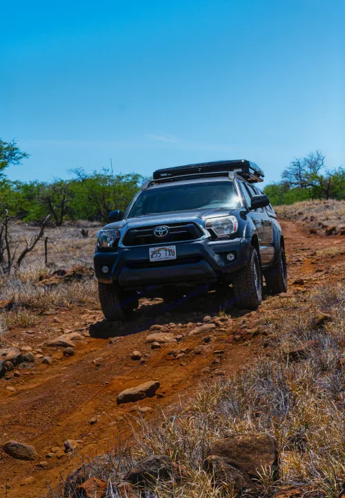 Rugged Toyota Tacoma truck with a rooftop tent tackles a rocky Hawaiian trail. An ideal adventure vehicle, more versatile than a typical RV rental.. Other Other 2013