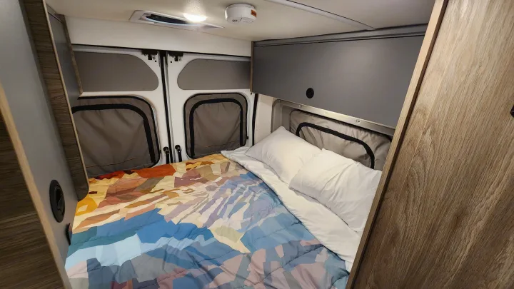 Cozy RV rental interior showcasing a comfortable bed with a vibrant comforter and practical overhead storage.. Winnebago Solis 2023