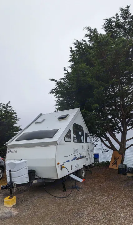 A Chalet A-frame camper, an excellent RV rental option, parked at a misty outdoor campsite.. Chalet Chalet Popup Trailer 2006