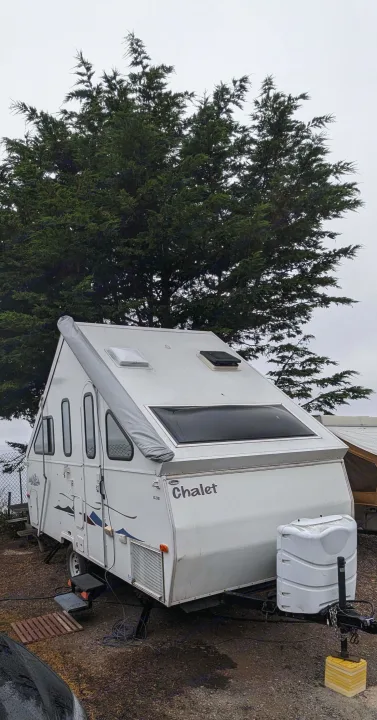 White Chalet A-frame RV rental, a pop-up camper, parked outdoors near a large tree.. Chalet Chalet Popup Trailer 2006
