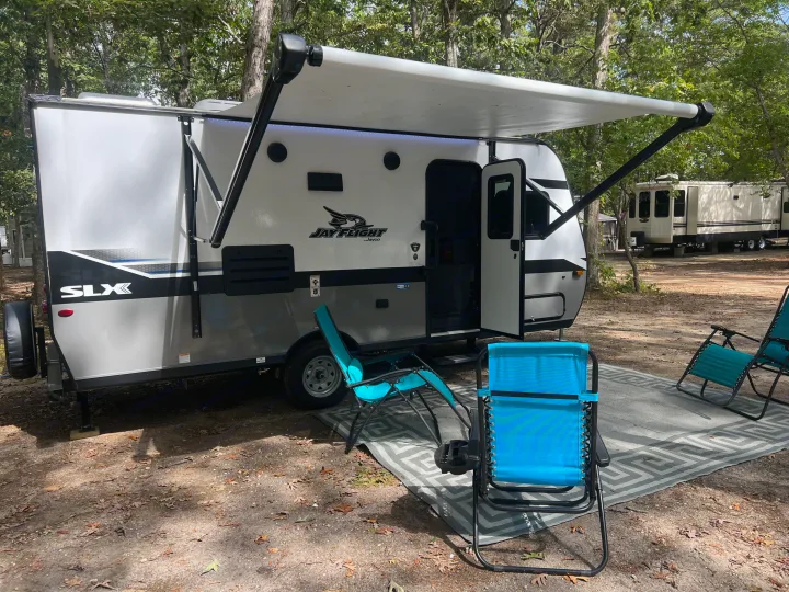 Relax at a serene campsite with this RV rental travel trailer, featuring an extended awning and outdoor chairs.. Jayco Jay Flight 2022