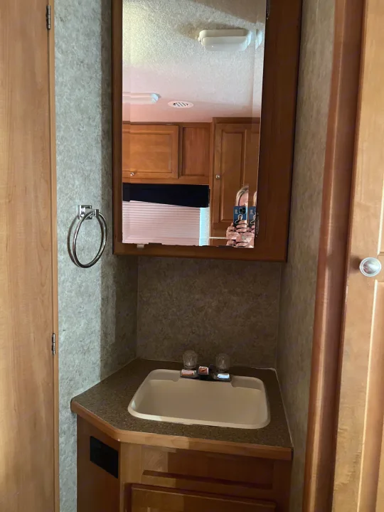 Compact RV rental bathroom featuring a sink, mirrored medicine cabinet, towel ring, and light wood cabinetry.. Winnebago Chalet 2010