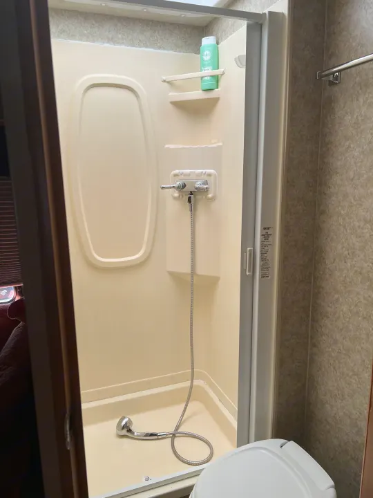 Compact RV rental bathroom featuring a shower with a flexible hose, shelf, shampoo, and a retractable door.. Winnebago Chalet 2010