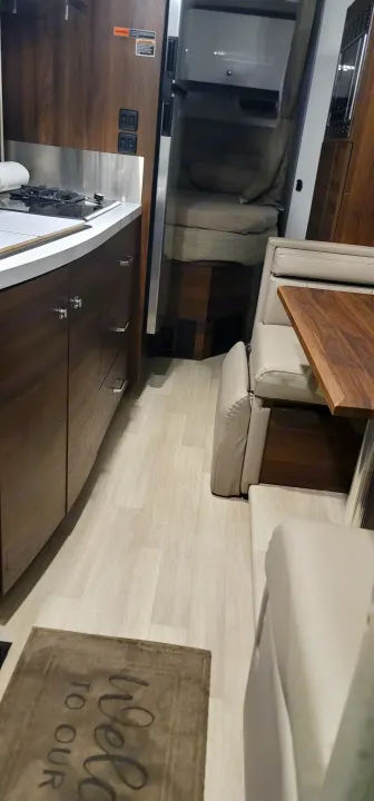Modern RV rental interior, showcasing a sleek kitchen, light-colored lounge seating, and wood-look flooring. Welcoming feel.. Winnebago Navion 2022