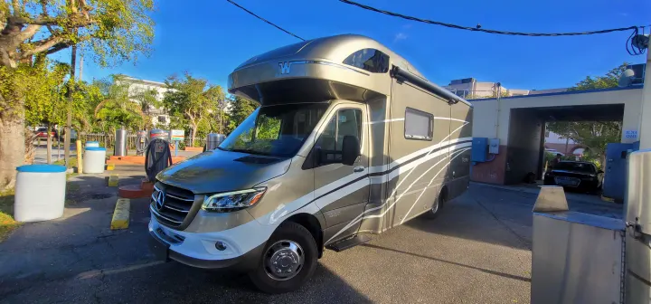A sleek Winnebago Class C rv rental at a car wash/detailing station. Vacuum islands and a drive-thru bay are visible.. Winnebago Navion 2022