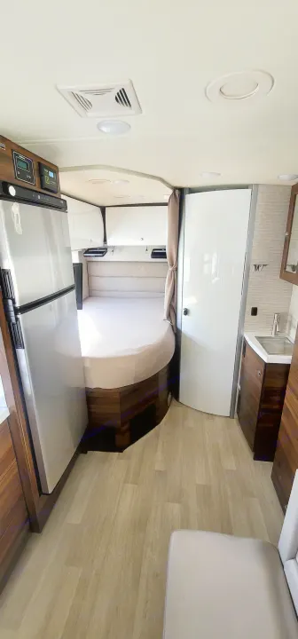 Spacious RV rental interior with a cozy bed, modern kitchenette, compact bathroom, and durable wood-look flooring.. Winnebago Navion 2022