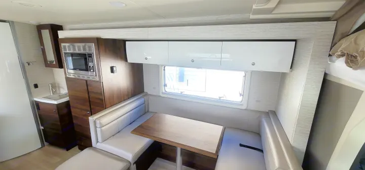 Modern RV rental interior with U-shaped dinette, compact kitchen, microwave, and white overhead cabinets.. Winnebago Navion 2022