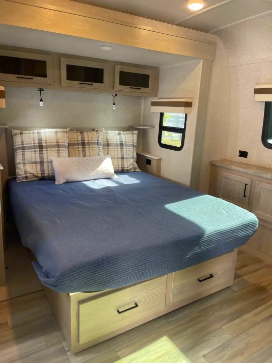 Spacious RV rental bedroom featuring a bed with plaid pillows, overhead cabinets, and under-bed drawers.. Forest River Rockwood Signature 2023