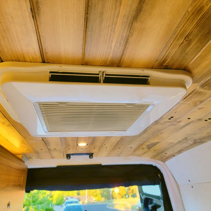 Inside an RV rental: a white roof-mounted AC unit provides climate control in this cozy space with a rustic wooden ceiling.. Mercedes-Benz Sprinter 2020