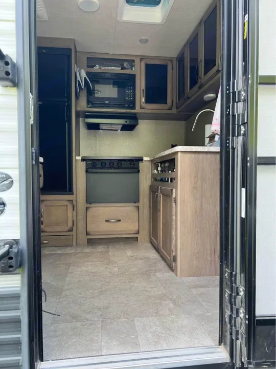 RV rental interior view: a neat, compact kitchen with fridge, stove, microwave, and sink, ideal for on-the-go living.. Grand Design Transcend Xplor 2020