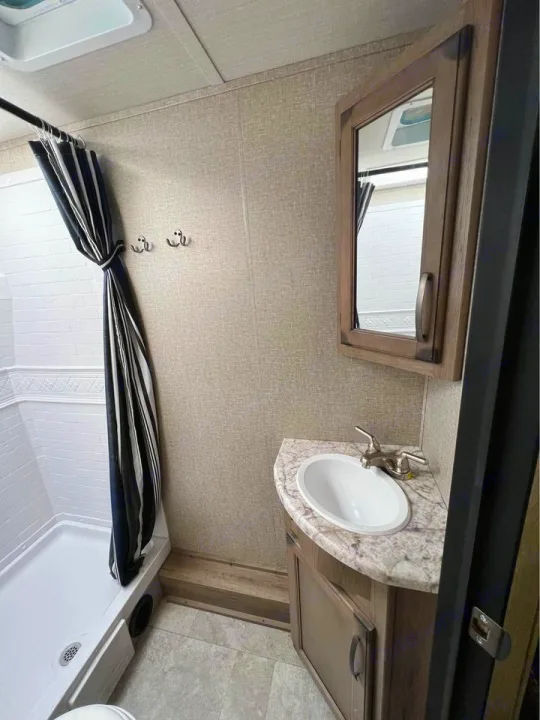 Clean RV rental bathroom. Features a shower with striped curtain, compact vanity with sink, mirror, and neutral tones.. Grand Design Transcend Xplor 2020
