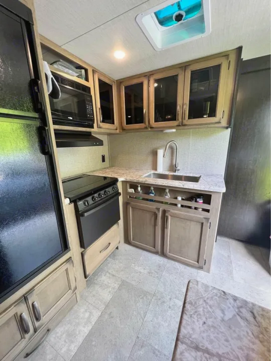 Step inside this clean, modern RV rental kitchen featuring a fridge, microwave, stove, sink, and sleek cabinetry.. Grand Design Transcend Xplor 2020