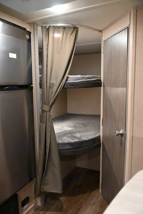 Cozy bunk beds with privacy curtains are featured in this rv rental, next to a refrigerator and interior door.. Coachmen Catalina Summit 184BHS 2022