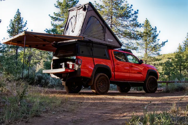 Adventure-ready red Toyota Tacoma truck with an open rooftop tent and awning. An ideal RV rental for overlanding and truck camping.. Toyota Tacoma TRD Pro 2023