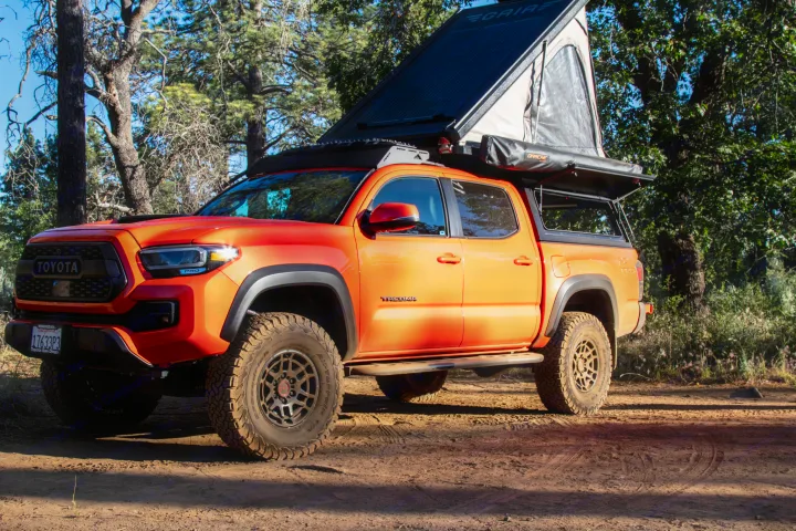Vibrant orange Toyota Tacoma with an open rooftop tent, perfect for an off-road RV rental camping adventure in the forest.. Toyota Tacoma TRD Pro 2023