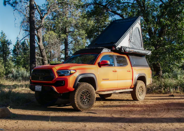 Orange Toyota Tacoma pickup truck with rooftop tent, ready for an RV rental camping adventure in the forest.. Toyota Tacoma TRD Pro 2023