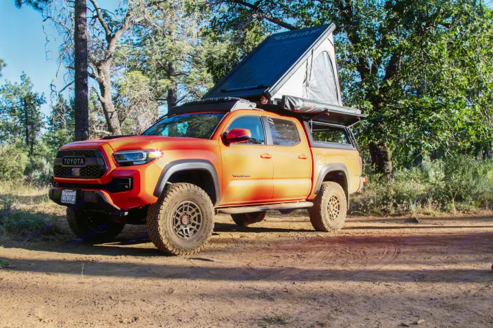Bright orange Toyota Tacoma truck with rooftop tent and awning on a dirt path; ideal for an RV rental.. Toyota Tacoma TRD Pro 2023