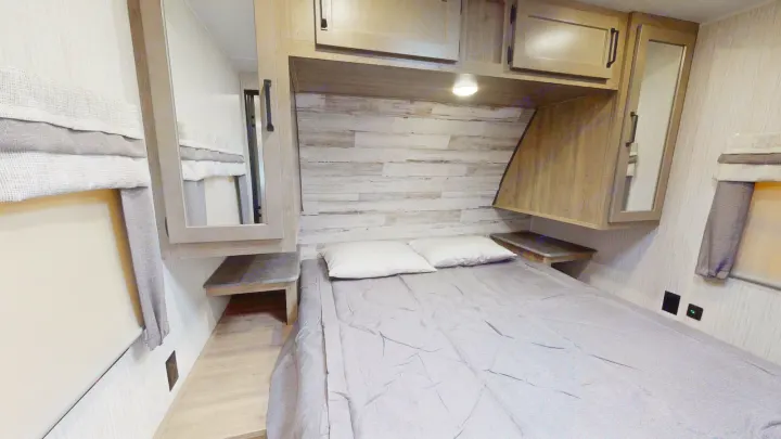 Cozy RV rental bedroom featuring a full-size bed, rustic headboard, overhead storage, and mirrored cabinets for compact living.. Forest River Palomino Puma 2023