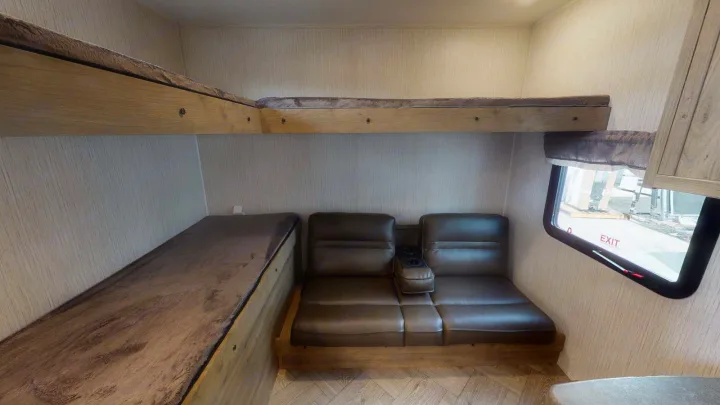 RV rental interior featuring a bunk bed over a lower sleeping area and a sofa with cupholders next to a window.. Forest River Palomino Puma 2023