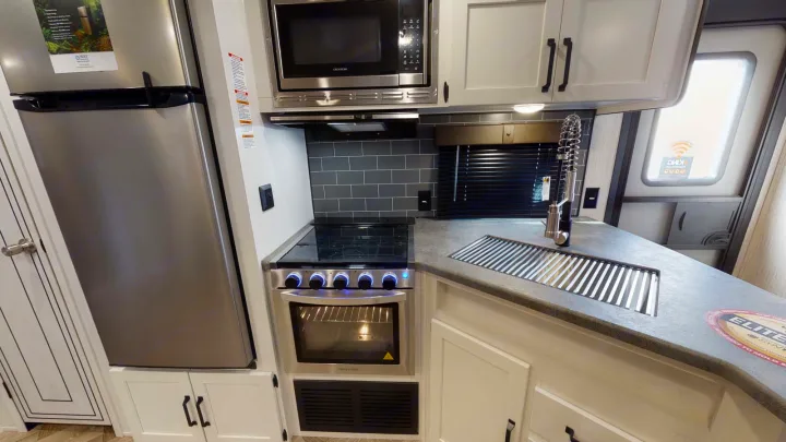 Modern RV kitchen setup with stainless appliances, stove, microwave, sink, and fridge. Perfect for your next rv rental adventure.. Forest River Palomino Puma 2023