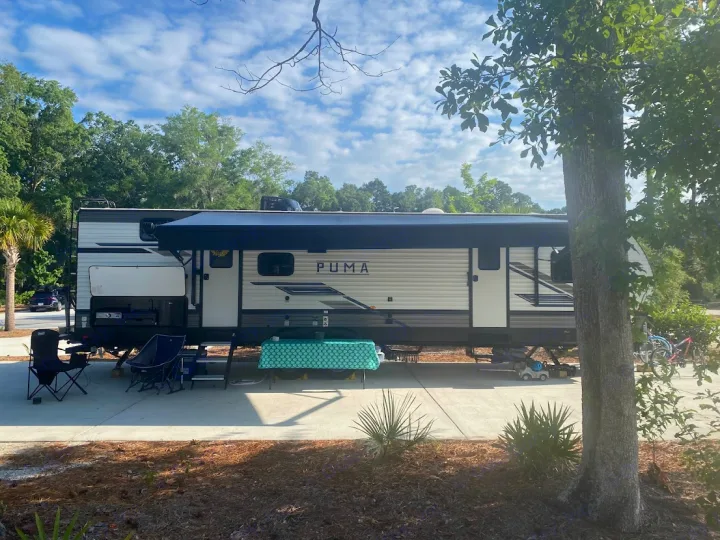 Relaxing at a sunny RV rental campsite with an extended awning, chairs, and outdoor kitchen setup.. Forest River Palomino Puma 2023